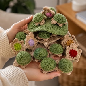 Puede incluir: Un sombrero de ganchillo en color verde oliva que presenta varias tortugas pequeñas de peluche adheridas a la superficie. El sombrero está adornado con varios detalles de ganchillo en forma de flor en colores como rosa, morado, amarillo y rojo.