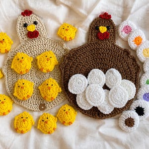 May include: Two crocheted chicken-shaped pouches, one beige and one brown, each with a red comb and yellow beak. The beige pouch is surrounded by ten small yellow crocheted chicks, while the brown pouch holds several white crocheted circles.