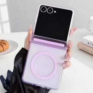 Könnte beinhalten: Eine faltbare Smartphone-Hülle in durchscheinendem Helllila. Die Hülle verfügt über einen markanten kreisförmigen Magnetring auf der unteren Rückseite und einen horizontalen Riegel über dem Scharnierbereich. Das Gerät hat zwei Kameralinsen.