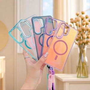 May include: A set of four rectangular smartphone cases with a gradient finish, featuring a circular magnetic ring on the back. The cases are translucent with blue, pink, purple, and orange hues, and include a braided wrist strap attached at the bottom.