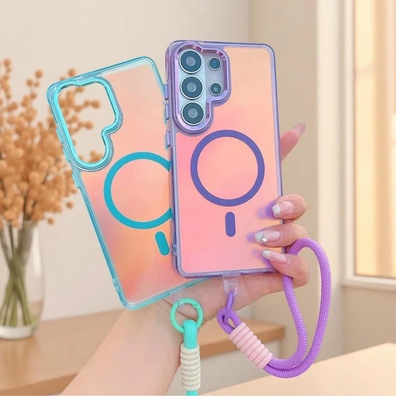May include: Two rectangular smartphone cases with a translucent iridescent finish. One case features a bright blue circular magnetic ring and a matching blue wrist strap. The other case has a purple circular magnetic ring and a purple wrist strap.