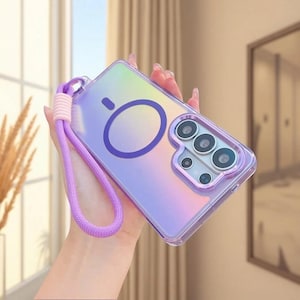 May include: A clear, iridescent purple smartphone case featuring a circular magnetic charging ring on the back, a raised camera lens protector, and a matching purple braided wrist strap with a light pink accent connector.