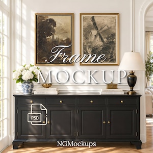 May include: Two rectangular gold frames containing sepia-toned landscape sketches hang above a long black wooden sideboard with four drawers and four doors featuring small gold knobs. A blue and white vase with white flowers sits on the left.