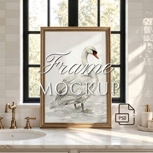 May include: A vertical rectangular gold-toned picture frame containing a watercolor-style illustration of a white swan standing in shallow water. The text "Frame MOCKUP" is overlaid in white script and sans-serif font across the center.