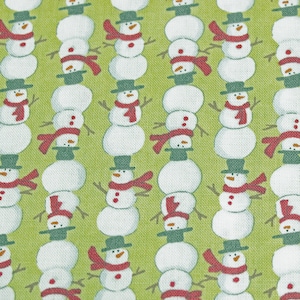 May include: A green fabric with a repeating pattern of white snowmen with red scarves and black hats. The snowmen are stacked in groups of three.