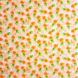 May include: A repeating pattern of orange pineapples with green leafy tops on a white background with a light orange brick-like pattern. The pineapples are evenly spaced and create a tropical theme.