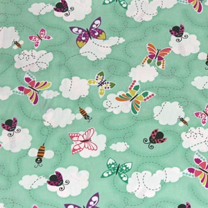 May include: A green fabric with a repeating pattern of butterflies, ladybugs, bees, and clouds. The butterflies are in various colors, including pink, purple, yellow, and blue. The ladybugs are red with black spots. The bees are yellow and black. The clouds are white.