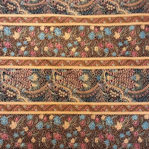 May include: A fabric with a repeating pattern of blue, pink, and yellow flowers on a brown background. The fabric has a border of gold and red.