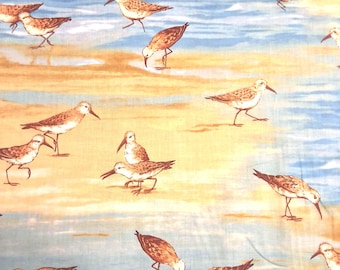 May include: A fabric pattern featuring numerous brown and tan sandpiper birds scattered across a background of light blue water and sandy yellow shorelines. The birds are depicted in various poses, including walking and foraging along the beach.