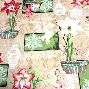 Op de afbeelding: Een beige stof met een herhalend patroon van rode en witte amaryllisbloemen in groene potten, witte sneeuwvlokillustraties, lijntekeningen van kerstballen en vintage ansichtkaarttekst met de zin Joy to the world.