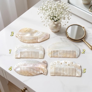 Könnte beinhalten: Fünf Haarkämme aus irisierendem Perlmutt, nummeriert von eins bis fünf. Die Kämme haben verschiedene Formen, darunter ein Vogel, ein Fisch sowie florale oder wolkenartige Schnitzereien, und sind neben einem kleinen Handspiegel angeordnet.