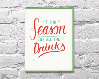 May include: A white card with a green border features a red and green handwritten message that reads "Tis' the season for all the drinks".