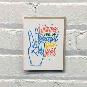 May include: A white card with a peace sign and the text "Wishing for a peaceful New Year" in colourful lettering.