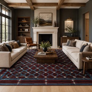 May include: A large rectangular area rug featuring a deep burgundy background with a repeating geometric lattice pattern in blue and small white square accents. The rug is positioned in a living room setting between two beige sofas and a wooden table.