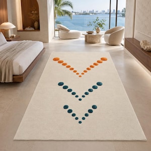 Peut inclure: Un tapis rectangulaire de couleur crème claire présentant une série d'accents circulaires touffetés disposés en trois motifs en chevron distincts. La rangée supérieure se compose de cercles orange, tandis que les deux rangées inférieures sont bleu sarcelle.