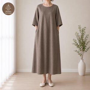 May include: A taupe-colored midi dress with a round neckline and elbow-length sleeves. The garment features a loose, straight-cut silhouette with side pockets and a subtle textured fabric finish. A circular badge displays the text DIGITAL PDF SEWING PATTERN.