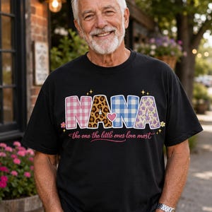 May include: A black short-sleeved t-shirt featuring the word NANA in large block letters with varied patterns including pink plaid, leopard print, blue gingham, and purple floral, with the text the one the little ones love most below.