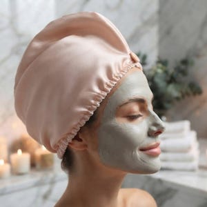 May include: A pale pink satin hair bonnet with a gathered elastic edge. The bonnet features a smooth, lustrous finish and a structured, rounded shape that covers the top of the head, providing a soft and protective covering for hair.