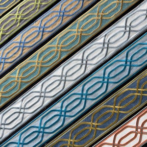 May include: A collection of decorative fabric trim strips arranged diagonally. Each strip features a repeating geometric lattice pattern created with raised corded lines in various colours including gold, blue, silver, green, and orange.