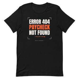 Könnte beinhalten: Ein schwarzes T-Shirt mit kurzen Ärmeln und weißem sowie orangefarbenem Text, der ERROR 404 PAYCHECK NOT FOUND lautet, ergänzt durch den kleineren Text > retry after coffee und PAID IN EXPOSURE, eingerahmt von vier Eckklammern in zentrierter Anordnung.