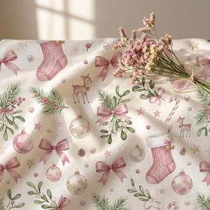 Könnte beinhalten: Ein cremefarbener Stoff mit einem wiederkehrenden Muster aus rosa gestrickten Strümpfen, Rehen, Tannenzweigen, Misteln, rosa Schleifen, Zuckerstangen und Weihnachtskugeln. Ein kleiner Strauß getrockneter rosa Blumen liegt auf dem Stoff.