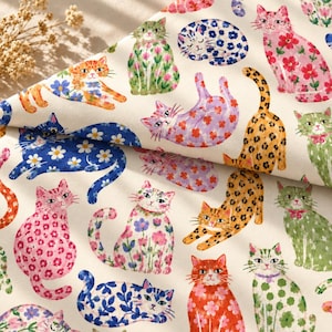 May include: A cream-coloured fabric featuring a repeating pattern of cats in various poses and colours. The cats are decorated with floral, leopard, and leaf prints in shades of pink, blue, green, orange, and yellow, with some cats sleeping.