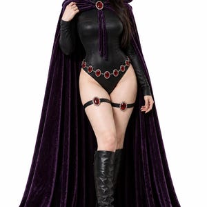 May include: A long purple velvet hooded cape with a red gemstone clasp, worn over a black long-sleeved bodysuit. The outfit includes a belt and two thigh garters, each featuring oval red gemstones set in silver-toned metal, paired with black boots.