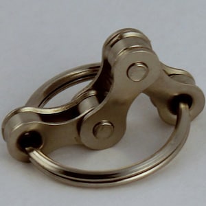 May include: A silver metal fidget toy with a chain link design. The toy has a ring that can be spun around the chain links.