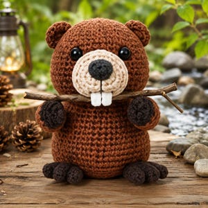 Puede incluir: Un castor de peluche tejido a ganchillo en color marrón con un hocico beige claro, dos dientes de fieltro blanco, una nariz gris oscuro y ojos de plástico negro. El castor sostiene una rama de madera natural fina horizontalmente con sus patas.