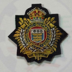 May include: A black embroidered military badge featuring a central shield with three circles and horizontal bars, surrounded by a blue garter with the text HONI SOIT QUI MAL Y PENSE, topped with a crown, and a banner at the bottom reading WE SUSTAIN.
