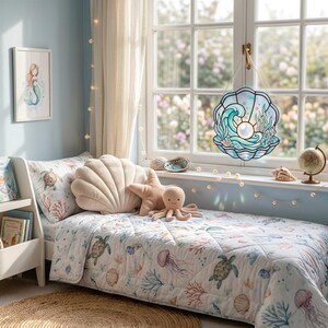 Puede incluir: Un atrapasoles de vidrieras con forma de concha marina con una perla central, olas azules y detalles de coral, colgado en una ventana. La habitaci&oacute;n cuenta con una cama con una colcha de tem&aacute;tica marina, un coj&iacute;n con forma de concha, una estrella de mar y un peluche de pulpo.