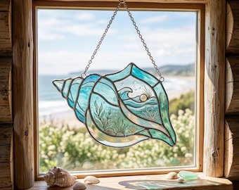 Puede incluir: Un atrapasoles de vidrieras con forma de caracola, que presenta tonos de vidrio azul y verde azulado con líneas de plomo. El diseño muestra una escena submarina con algas, una ola y una pequeña esfera blanca, suspendido por una cadena metálica.