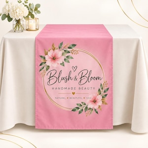 Könnte beinhalten: Ein rosafarbener Tischläufer mit einem goldenen kreisförmigen Rahmen, der mit rosa Blumen und grünen Blättern im Aquarellstil verziert ist. Der Text lautet Blush & Bloom HANDMADE BEAUTY mit dem Slogan NATURAL BEAUTIFUL YOU, ergänzt durch kleine Herzen.