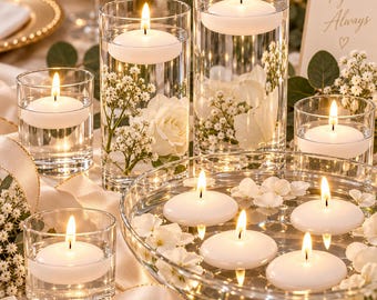 May include: A collection of clear glass cylinders and a shallow bowl filled with water, each containing a white floating candle. The arrangements are decorated with white roses and baby's breath flowers, creating a bright, illuminated display.