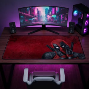 Peut inclure: Un tapis de bureau rectangulaire avec un fond rouge texturé et une illustration graphique du personnage Deadpool en costume noir et rouge, placé sur la droite avec les mains près du visage et deux poignées de katana visibles derrière.