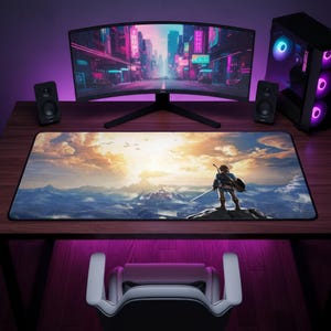 May include: A rectangular desk mat featuring a printed illustration of a character standing on a cliff overlooking a mountainous landscape at sunset. The mat has a black border and is positioned on a wooden desk in front of a computer monitor.