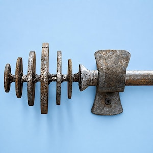 May include: A metal curtain rod finial featuring a series of five graduated circular discs welded to a central rod, connected to a wall-mounted bracket with a visible screw. The metal has a weathered, textured, and rusted brown and grey finish.