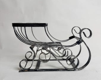May include: Black metal decorative sleigh with a flat top and curved runners. The sleigh features a wire basket design and decorative scrollwork on the sides. A vintage-style decorative piece.