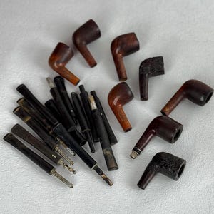 May include: An assortment of vintage tobacco pipes and stems. The pipes are made of dark brown wood with curved stems. The stems are black and silver. The pipes vary in size and shape, with some showing signs of wear.