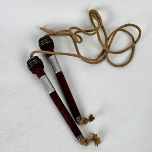 May include: A vintage jump rope with dark brown wooden handles, silver metal accents, and a tan rope. The handles have a ribbed design near the top. The rope is knotted at the ends of the handles.