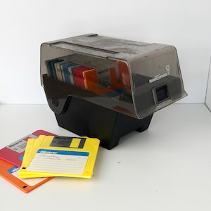 May include: A black plastic storage case with a translucent dark gray hinged lid featuring the Egghead Software logo, containing multiple colorful 3.5-inch floppy disks. Three additional yellow, red, and orange floppy disks lie in the foreground.