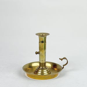 May include: A white ceramic mug with a black handle and the text "But First, Coffee" in a black, handwritten-style font. The mug is on a white surface.