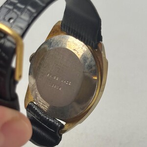 May include: Vintage gold-toned wristwatch with a black leather band. The watch face is not visible, but the back of the watch is visible, with the words "SWISS MADE" and the number "13826" engraved on the metal casing.