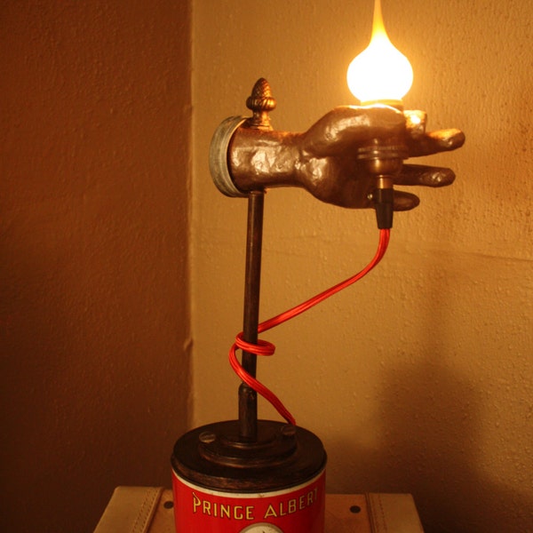 Unique handheld flame tip bulb lamp atop vintage Prince Albert tobacco can.
