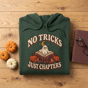 Könnte beinhalten: Ein dunkelgrüner Kapuzenpullover mit einem Grafikdruck eines Geistes, der ein offenes Buch liest, umgeben von Kürbissen und Herbstblättern. Der Text "NO TRICKS JUST CHAPTERS" ist in einer geschwungenen Schrift über und unter dem Motiv gedruckt.