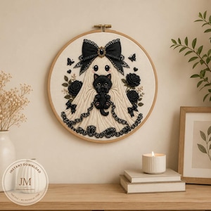 May include: A circular embroidery hoop containing a cream-colored fabric with a stitched design of a ghost wearing a large black bow, holding a small black kitten. The design includes black roses, small butterflies, and lace-like trim details.