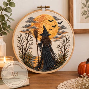 Può includere: Un ricamo circolare su telaio raffigurante una strega con un abito nero e un cappello a punta che tiene in mano una scopa. La scena mostra una grande luna gialla, nuvole scure, pipistrelli in volo e alberi spogli su uno sfondo in tessuto color crema.