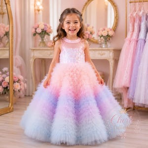 May include: A floor-length sleeveless dress featuring a bodice with a subtle floral pattern and a voluminous skirt made of layered tulle ruffles. The dress displays a gradient colour transition starting from pale pink at the top to blue at the hem.