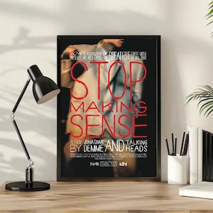 May include: A framed movie poster for Stop Making Sense, featuring a blurred figure in a light-colored suit against a black background. The title is printed in large red letters, with additional white text detailing the film and A24 production.