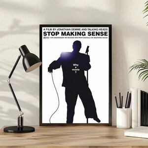 May include: A framed movie poster for Stop Making Sense, a film by Jonathan Demme and Talking Heads. The poster features a black silhouette of a person holding a microphone on a white background with the text Why a movie? in the center.